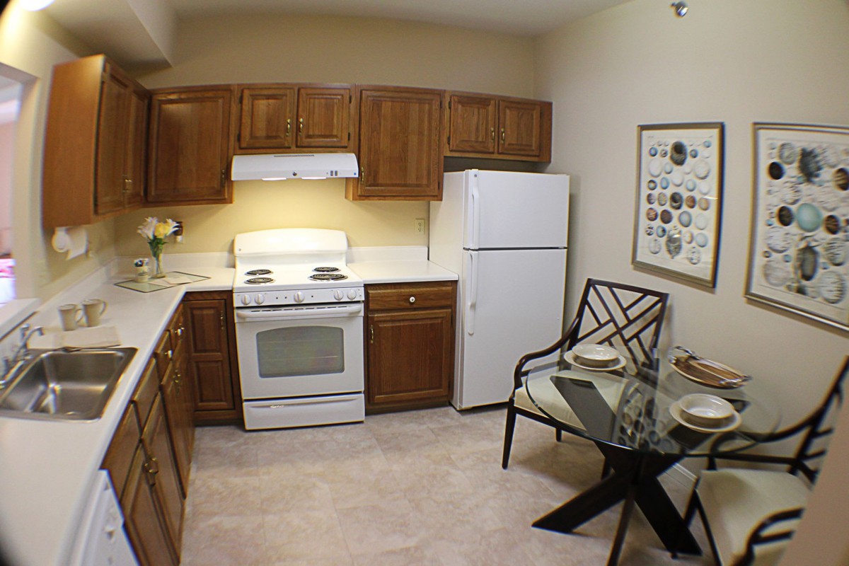 A cozy kitchen with wooden cabinets, a stove, refrigerator, and a small dining table.