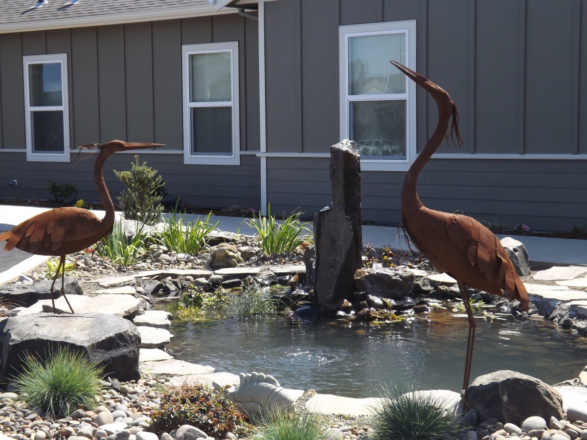 A garden scene with a pond, surrounded by decorative bird statues and landscaping elements.