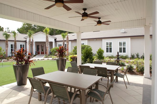 A covered outdoor patio with dining tables and chairs, overlooking a landscaped garden.