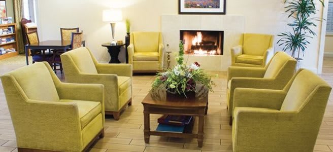 A cozy living room with yellow armchairs and a fireplace, featuring a wooden coffee table adorned with decorative plants.