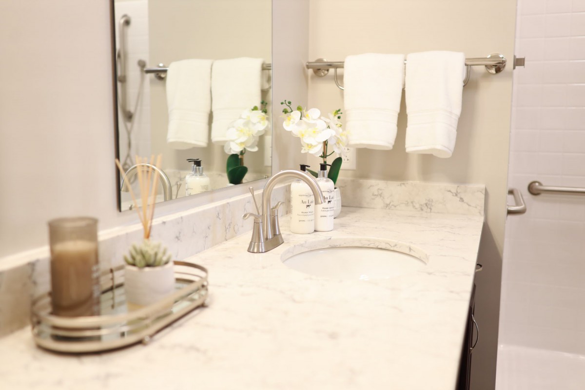 A clean and elegant bathroom with a marble countertop, featuring a sink, mirror, neatly hung towels, and decorative plants.
