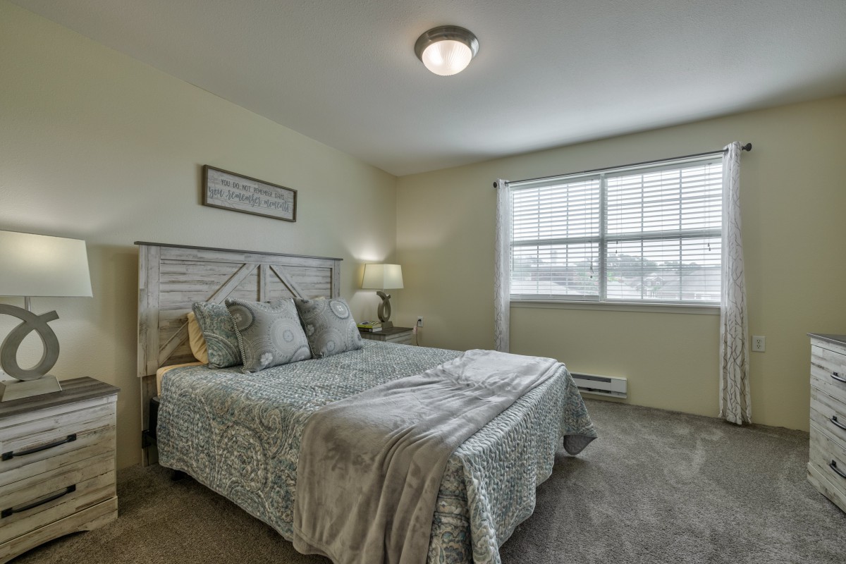 A cozy bedroom with a neatly made bed, soft lighting, and natural light streaming through the window.