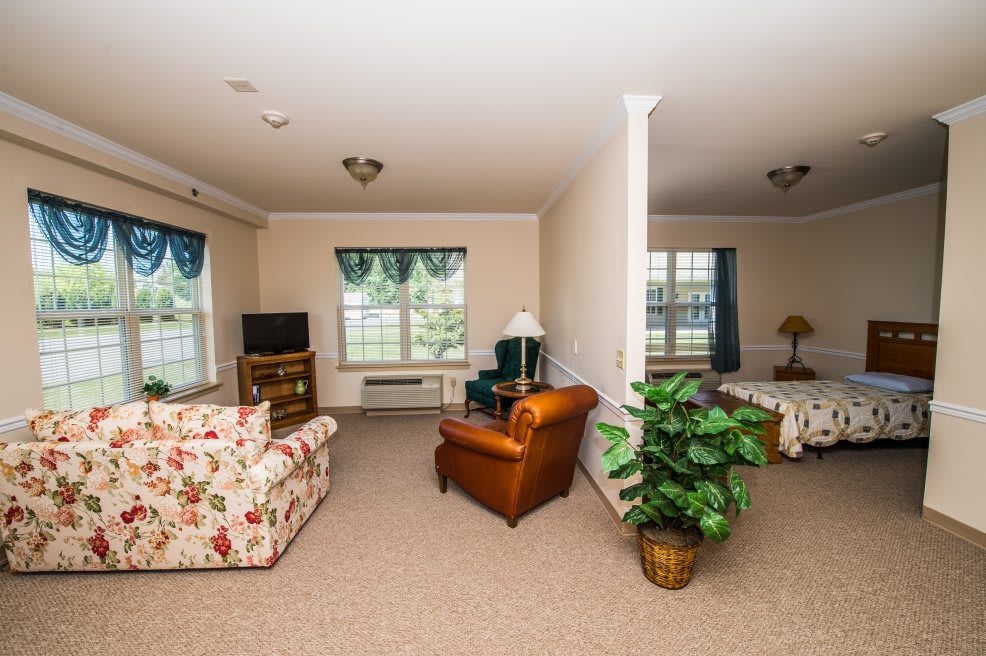 A cozy living room with floral and leather seating, featuring a TV and large windows.