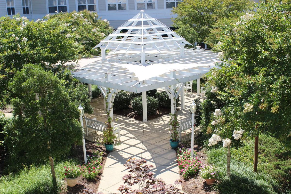 A white gazebo in a lush garden setting with surrounding trees and pathways.