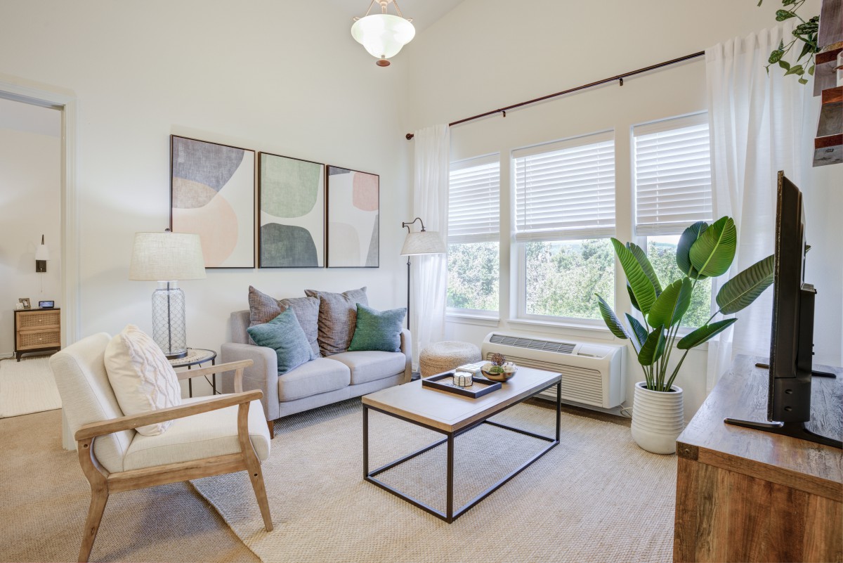 A modern and minimalist living room with a neutral color palette, featuring a comfortable sofa, a sleek coffee table, large artwork on the wall, and abundant natural light from the windows.