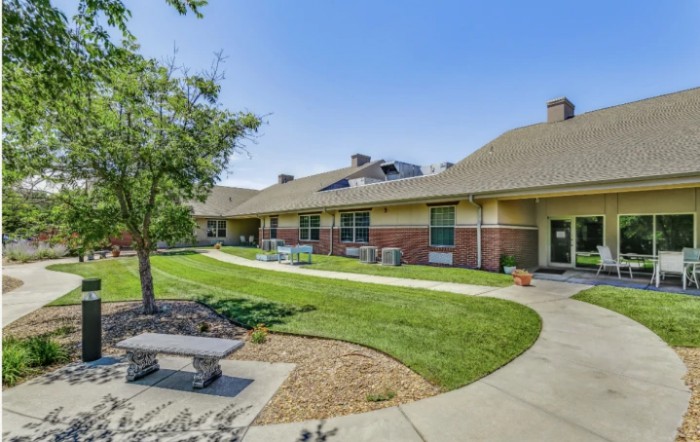 A peaceful outdoor area with a pathway, benches, and green lawn in front of a building.