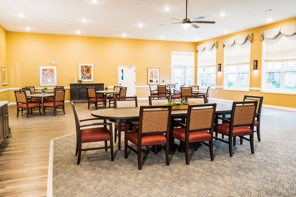 A spacious dining area with multiple tables and chairs, featuring bright orange walls and ample natural light.