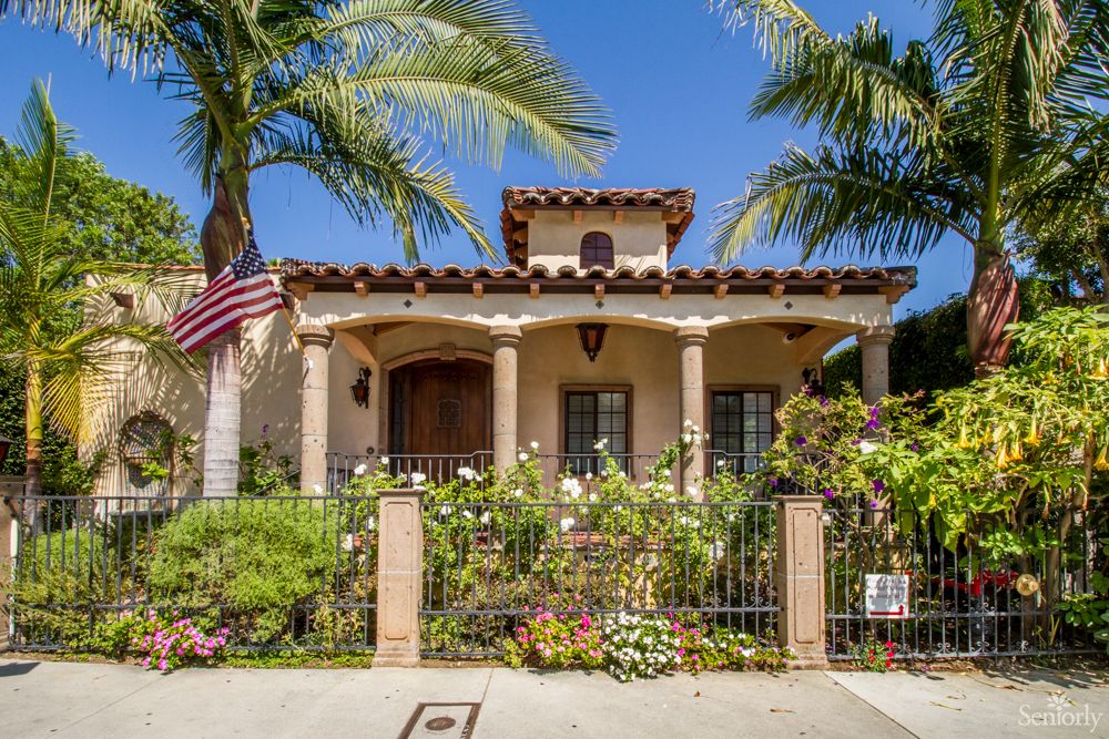 A beautiful house with a lush garden and palm trees on a sunny day.