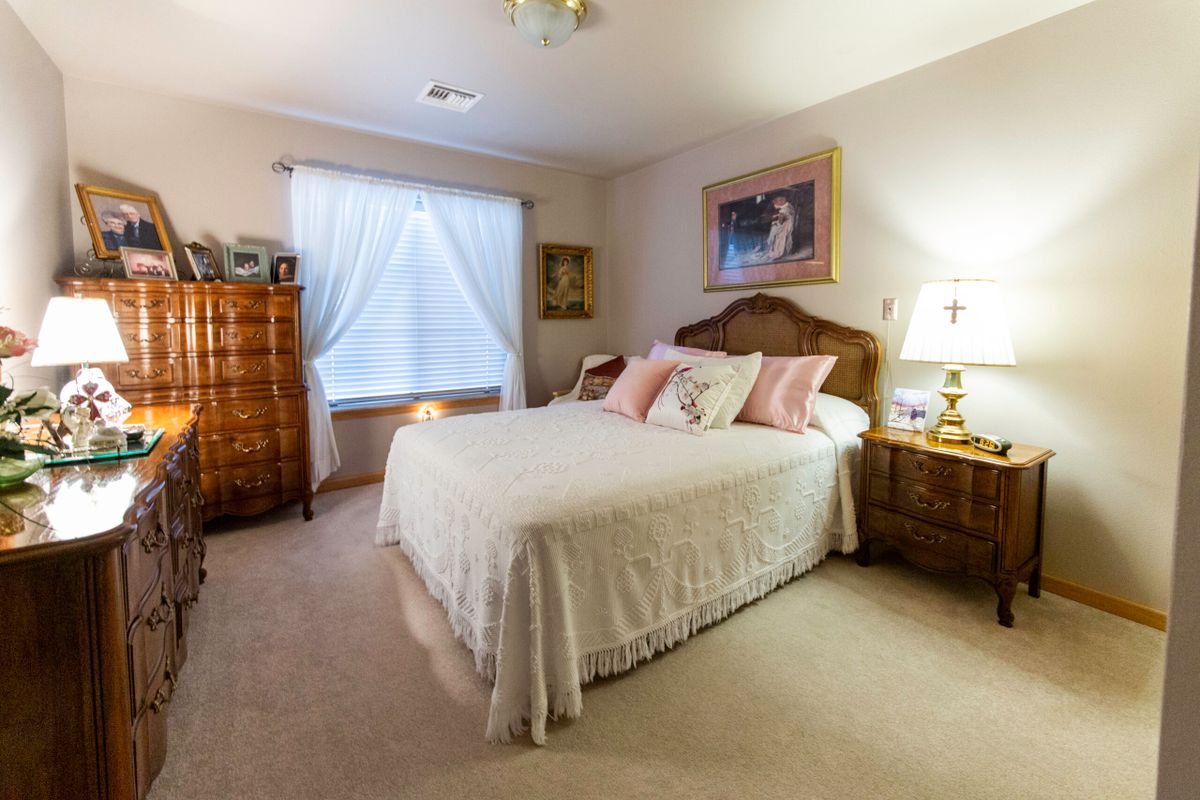 A cozy bedroom with a neatly made bed, wooden furniture, and a window covered by curtains.