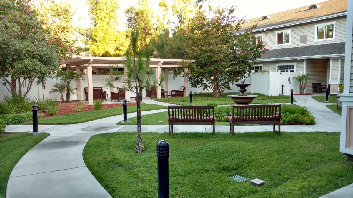 A tranquil garden area with benches, a fountain, and pathways surrounded by greenery.