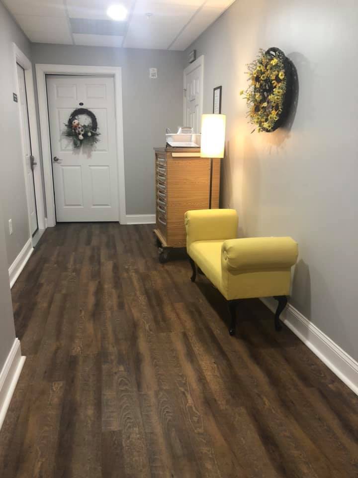 A modern hallway featuring wood flooring, a yellow bench, decorative wall art, and ambient lighting.