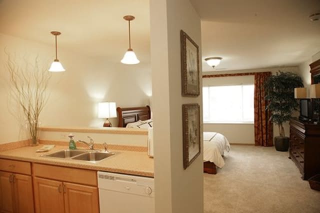 A cozy hotel room featuring a kitchen area with a sink and dishwasher, and a comfortable bedroom.