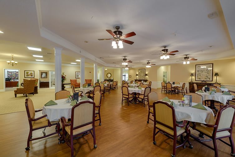 A spacious dining room with neatly arranged tables and chairs, ceiling fans, and warm lighting.