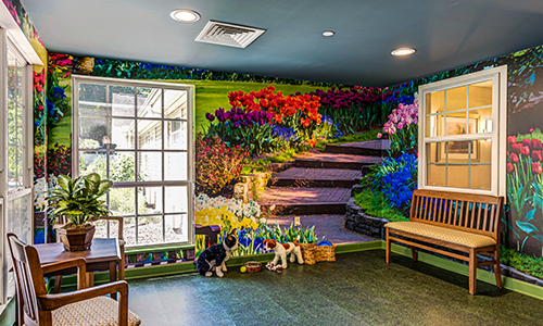 A vibrant indoor mural depicting a garden scene with colorful flowers and a staircase, accompanied by benches and large windows.