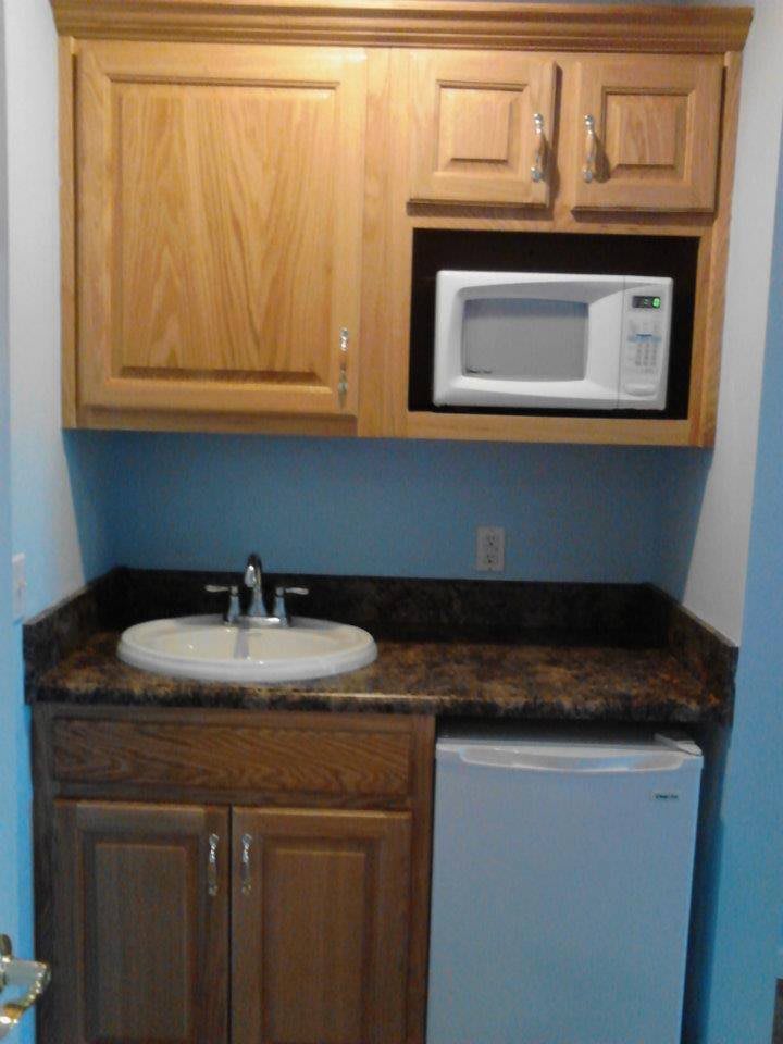 A compact kitchen area with a sink, microwave, cabinets, and a small refrigerator.