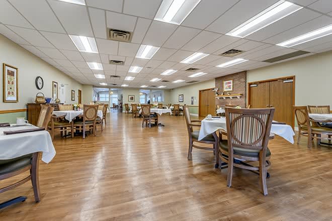 A spacious dining room featuring wooden floors and arranged tables and chairs.