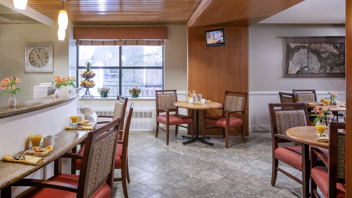 A cozy dining area with tables and chairs, featuring a large window and a wall-mounted television.
