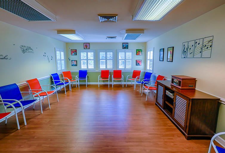 A spacious waiting room with colorful chairs against the walls, featuring a hardwood floor and ample natural light.