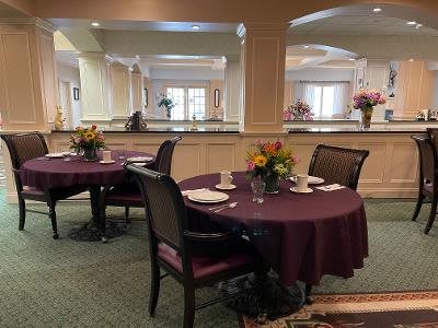A neatly set dining area with round tables, decorated with floral centerpieces.