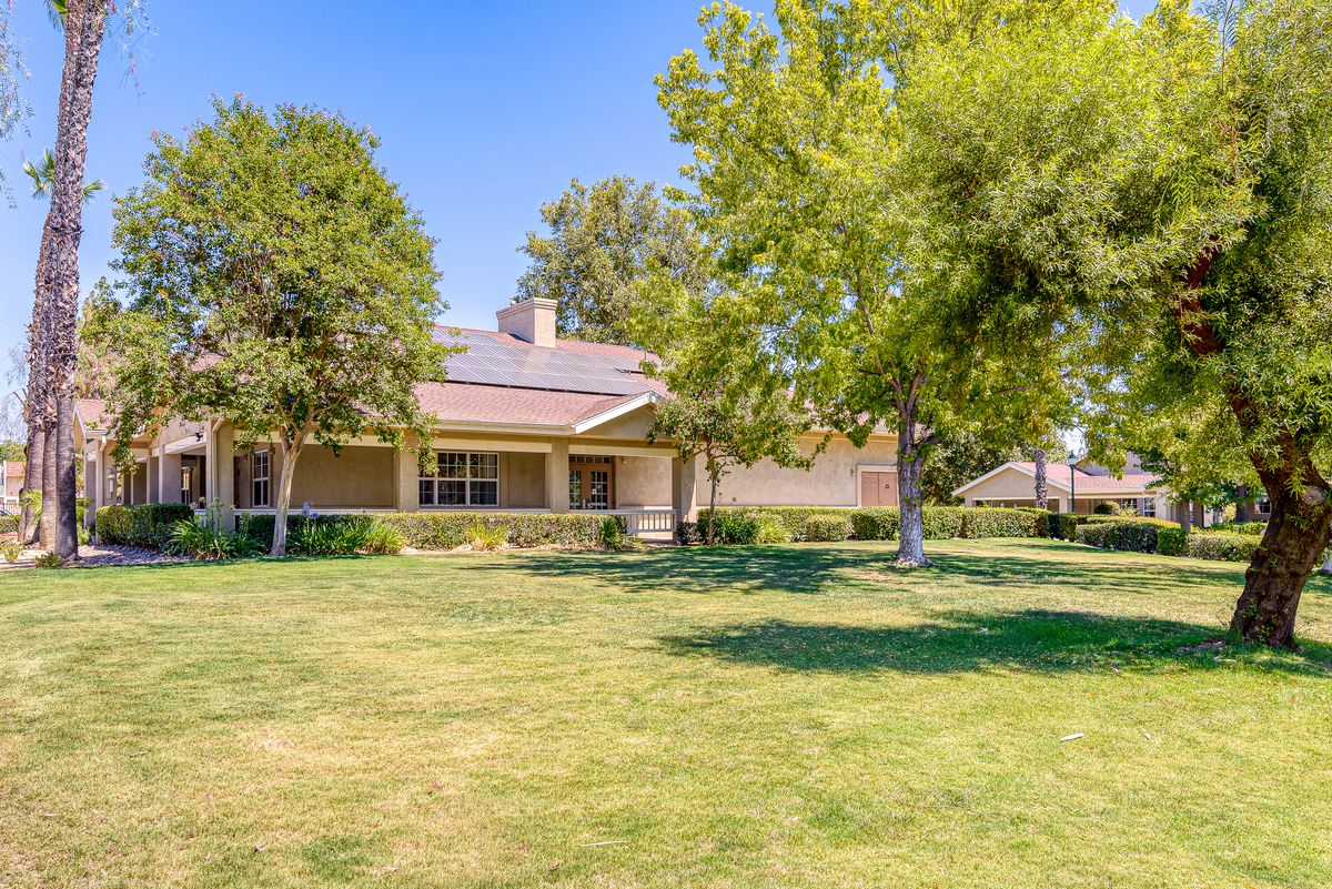 A single-story house with a large front lawn and surrounding trees on a sunny day.