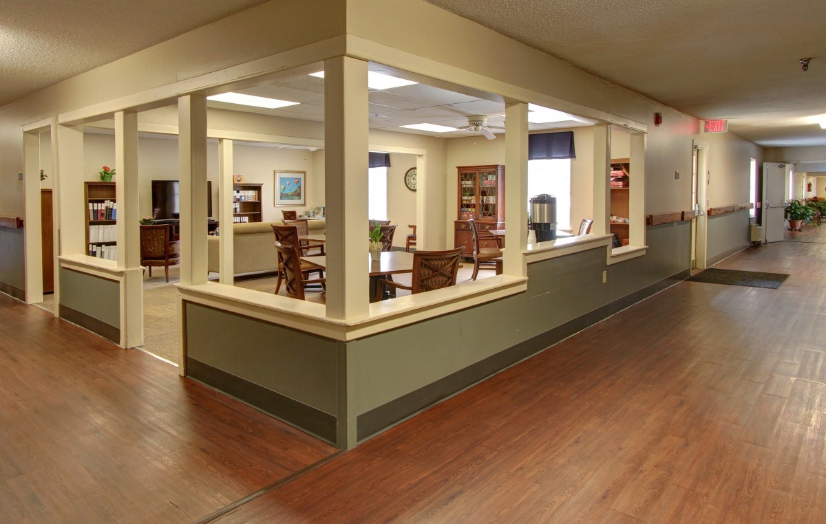 A view of a spacious interior room with chairs and tables arranged neatly, surrounded by large windows and a hardwood floor.
