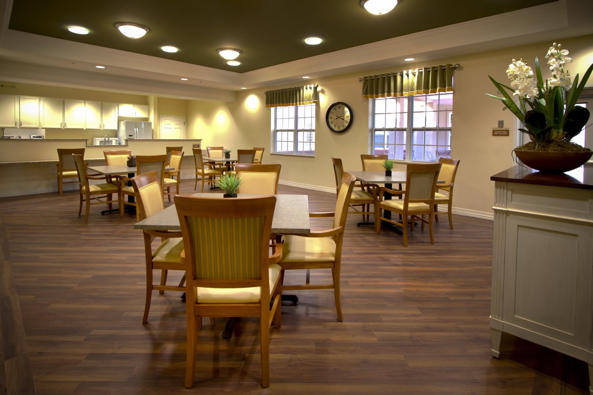 A well-lit dining area with wooden chairs and tables, featuring large windows.