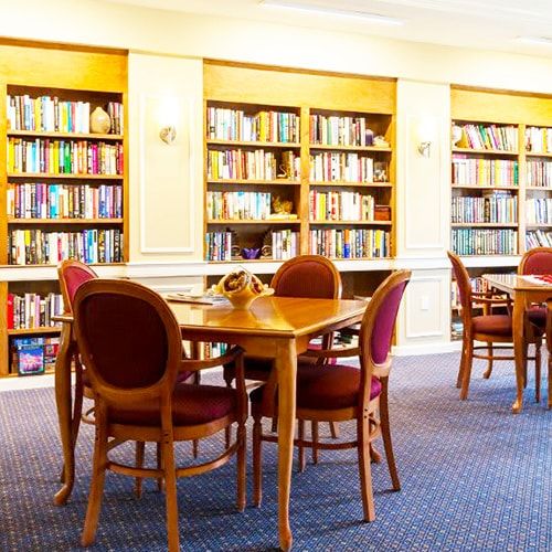 A well-lit library interior with bookshelves, tables, and chairs.