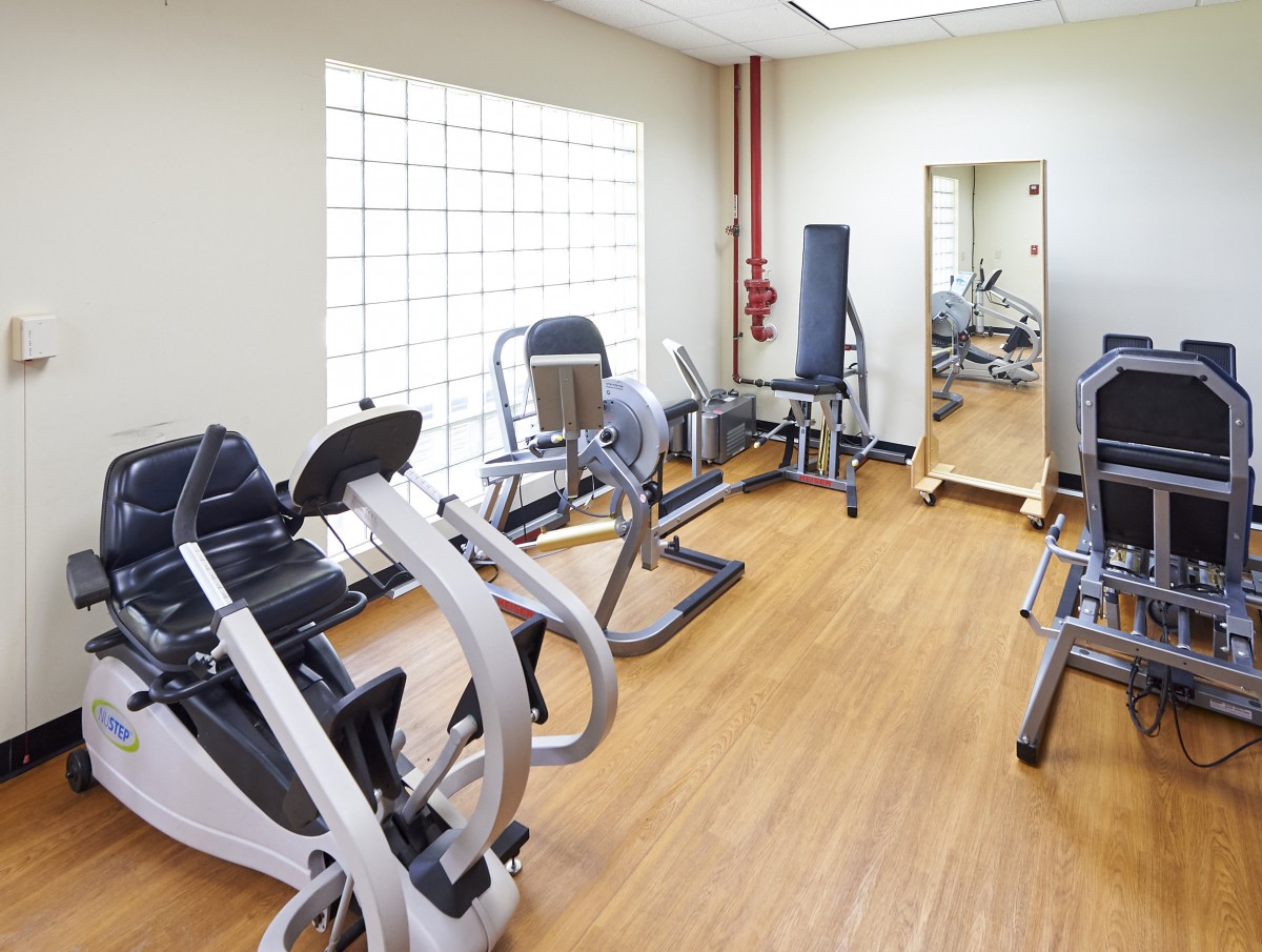 A well-equipped gym with various exercise machines and a large mirror on a wooden floor.