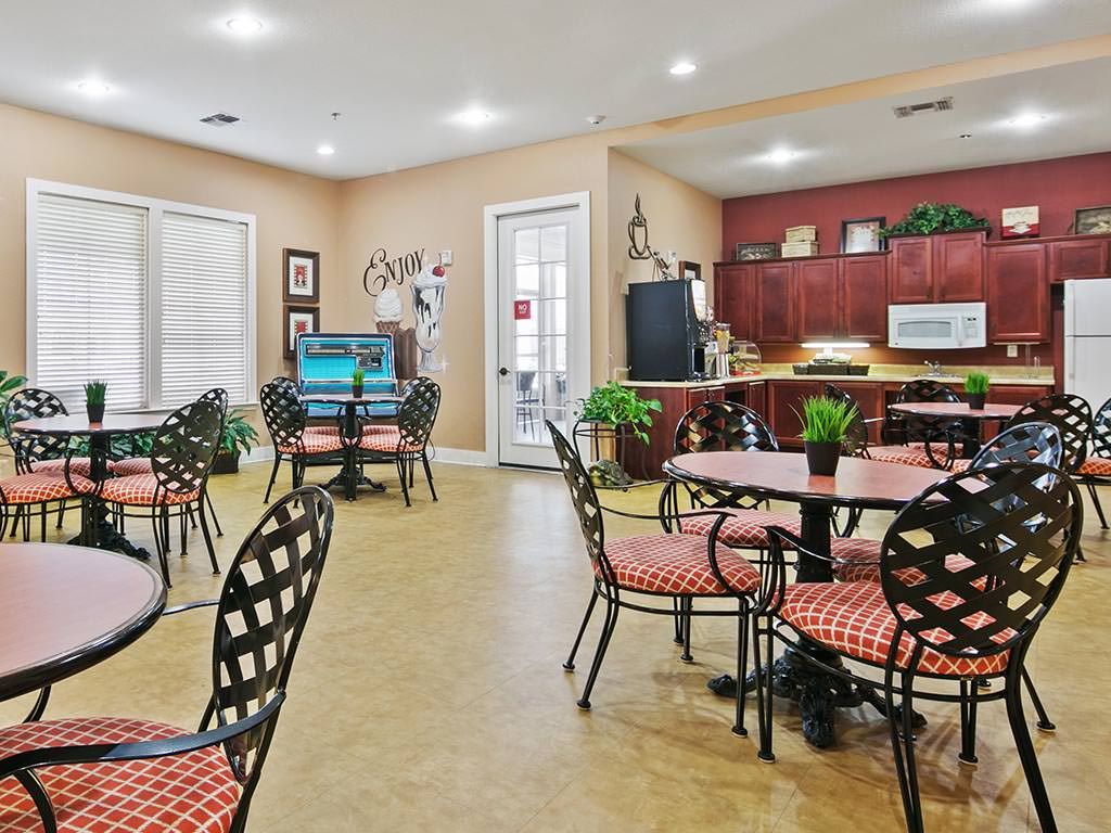 A cozy dining area with tables and chairs, featuring a small kitchen and decorative plants.