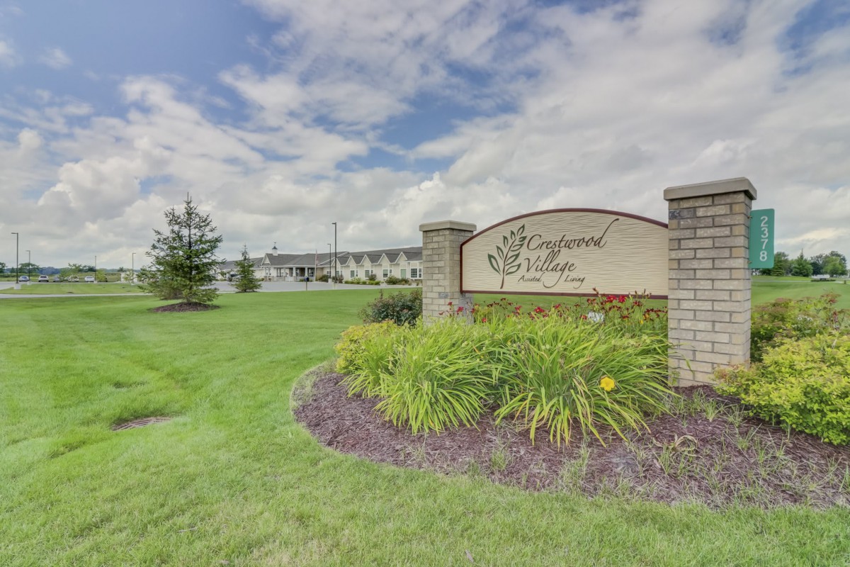 Entrance sign with landscaping and a building in the background under a cloudy sky.