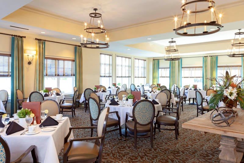 An elegant dining room with neatly arranged tables and chairs, illuminated by chandeliers.