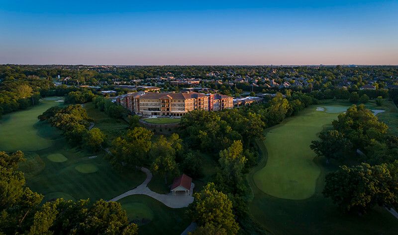 A stunning aerial view of a stadium surrounded by lush greenery and a golf course at sunset in an urban setting.