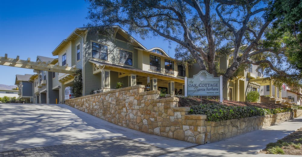 A two-story building with a stone wall and trees in the background.