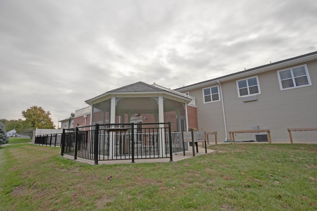 A backyard featuring a fenced gazebo adjacent to a house under a cloudy sky.