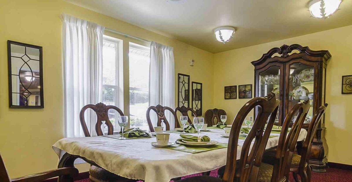 A cozy dining room with a table set for a meal, featuring elegant wooden chairs and natural light streaming through the windows.