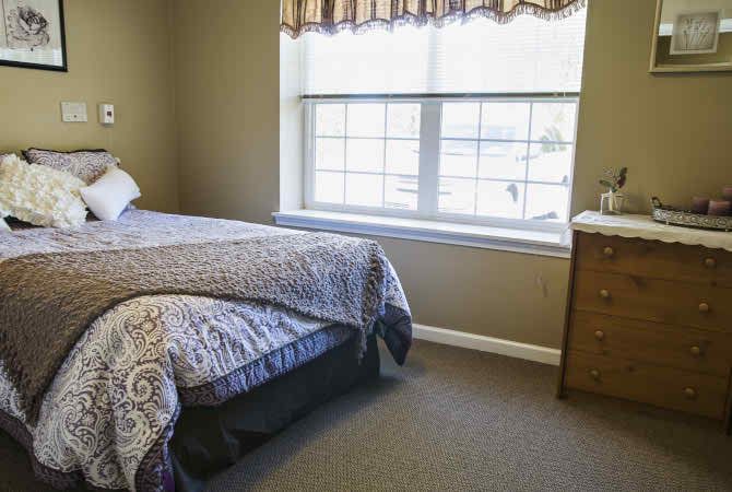 A cozy bedroom with a bed, dresser, and a large window.