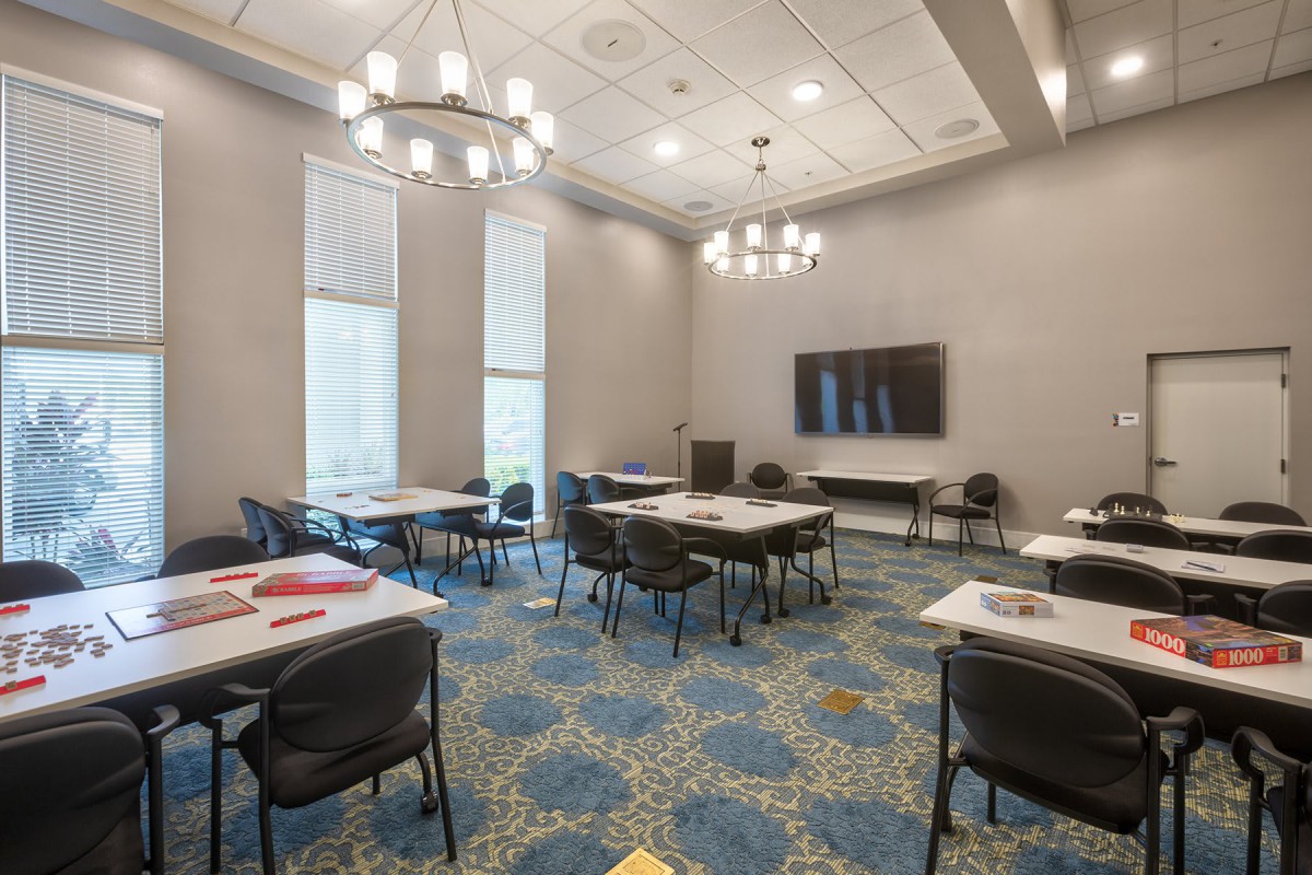 A modern conference room with arranged tables and chairs, featuring chandeliers and a projector screen.