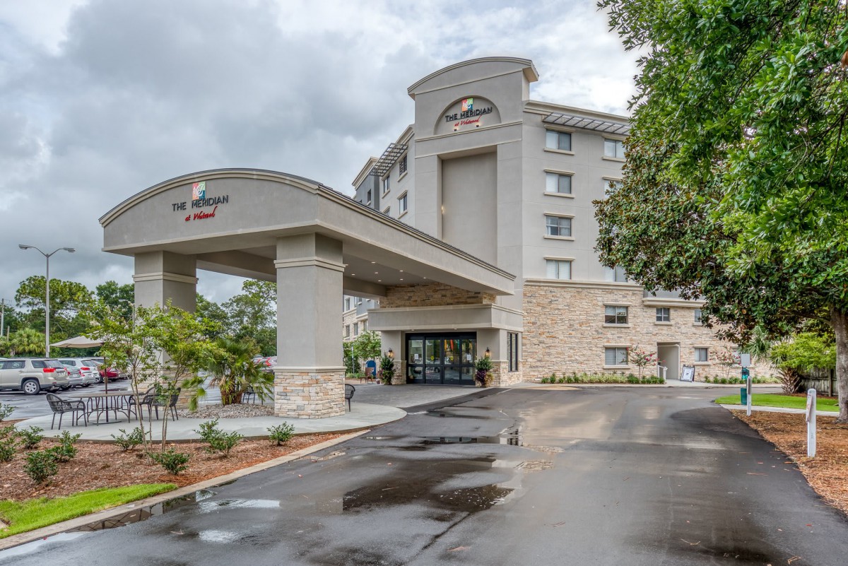 A modern hotel building with a grand entrance and surrounding greenery under a cloudy sky.