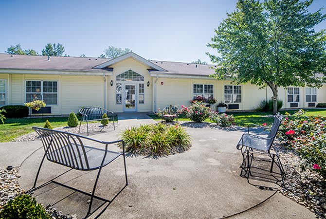 A sunny view of a building with a patio area featuring chairs and benches surrounded by a small garden.