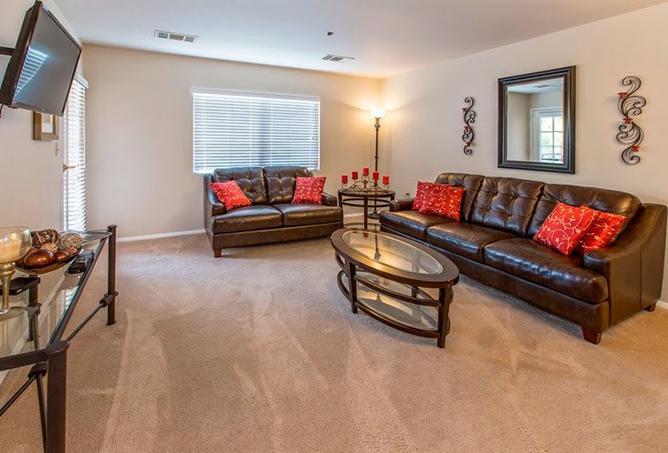 A modern living room with brown leather sofas, a glass coffee table, and red accent pillows.