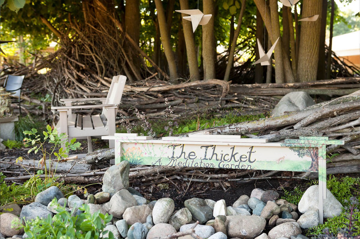 A rustic wooden bench and sign reading 'The Thicket' surrounded by rocks and paper cranes in a forest setting.