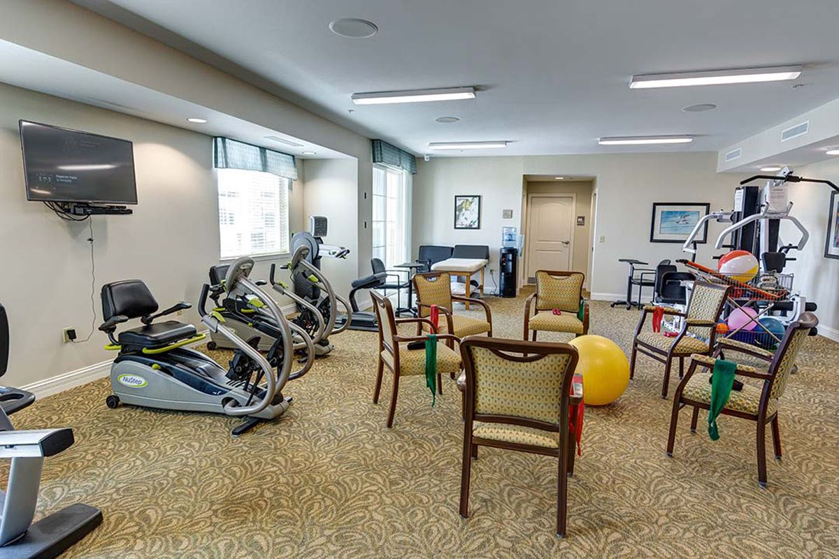 A fitness room equipped with exercise machines, chairs, and a therapy ball.