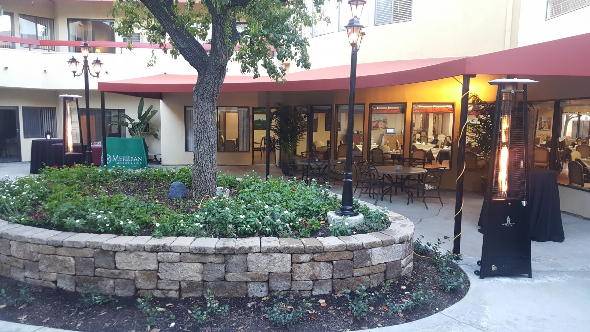 A charming courtyard with a stone wall and outdoor seating, surrounded by greenery and trees.