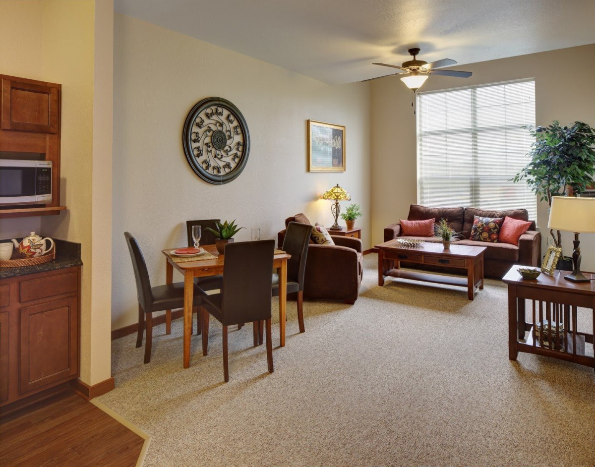 A cozy living room with a dining area, featuring comfortable seating, a coffee table, and a large window allowing natural light.