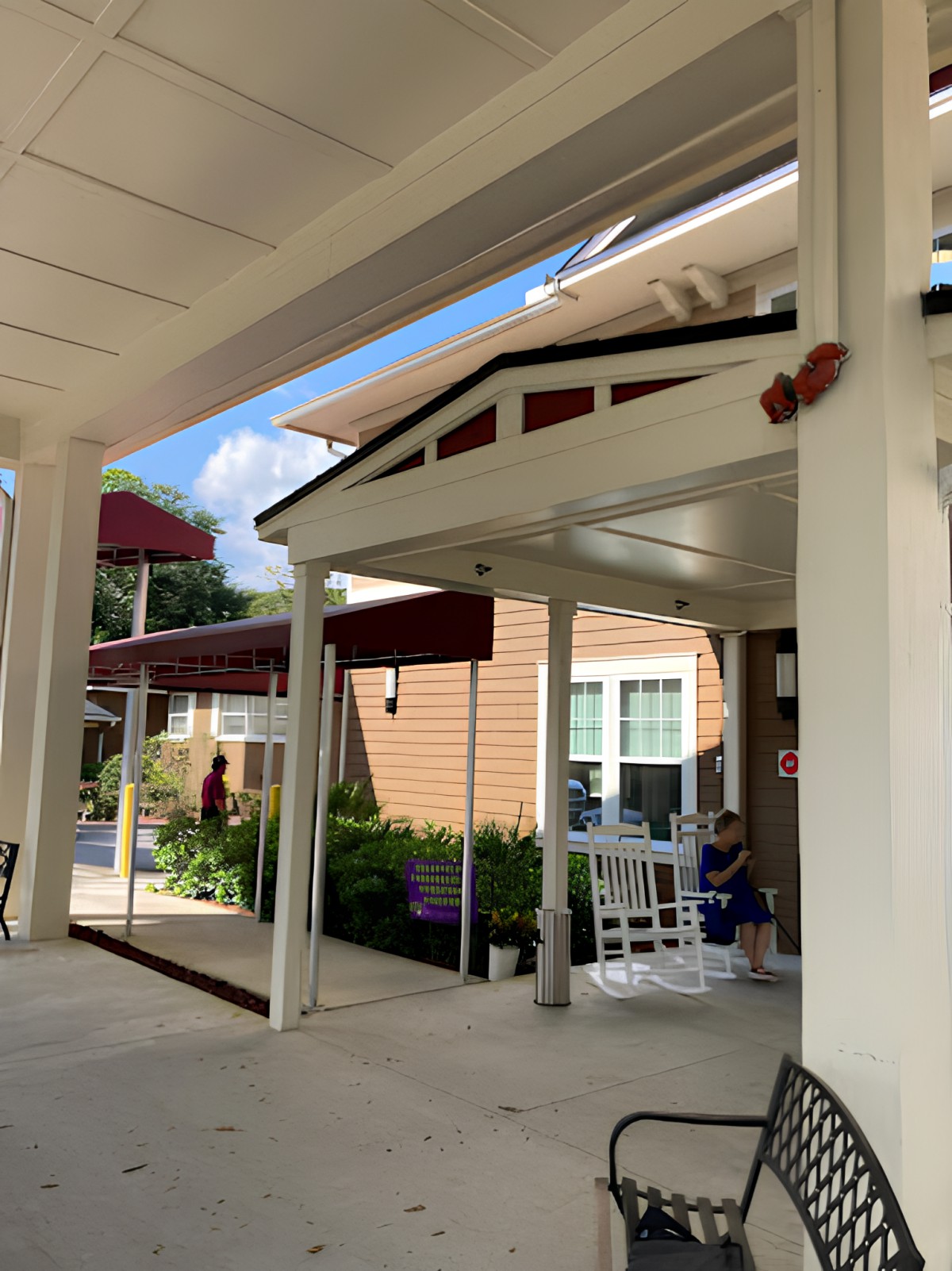 An inviting porch with white rocking chairs in front of a building under a clear blue sky.