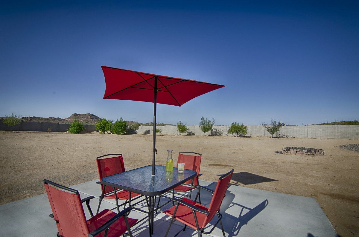 A patio set with red umbrella and chairs in a desert setting.