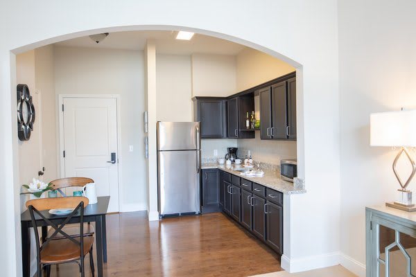 A modern kitchen with dark cabinets, stainless steel appliances, and wooden floors.