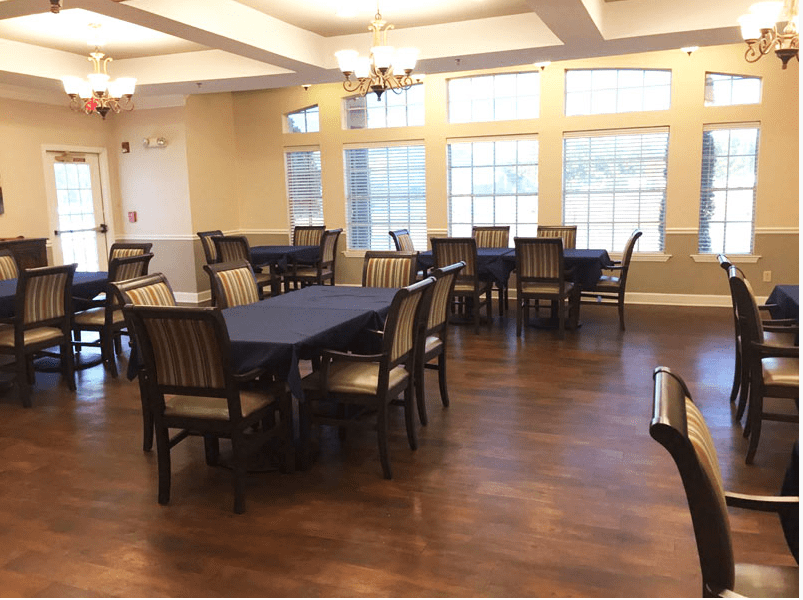 A spacious dining room with multiple tables and chairs, featuring large windows and wooden flooring.