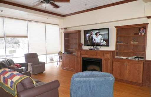 A cozy living room featuring comfortable seating, a television mounted above a fireplace, and wooden bookshelves.
