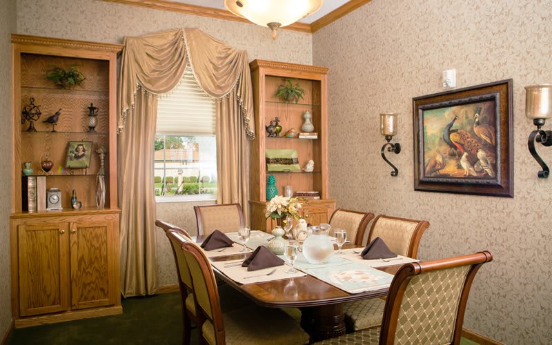An elegantly decorated dining room with a well-set table, featuring plush curtains and framed artwork.